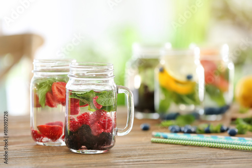 Mason jars of infused water with berries on wooden table