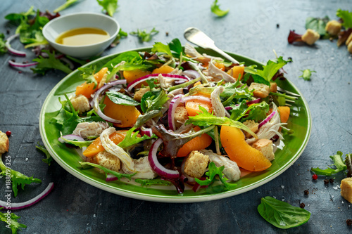 Fresh salad with chicken breast, peach, red onion, croutons and vegetables in a green plate. healthy food