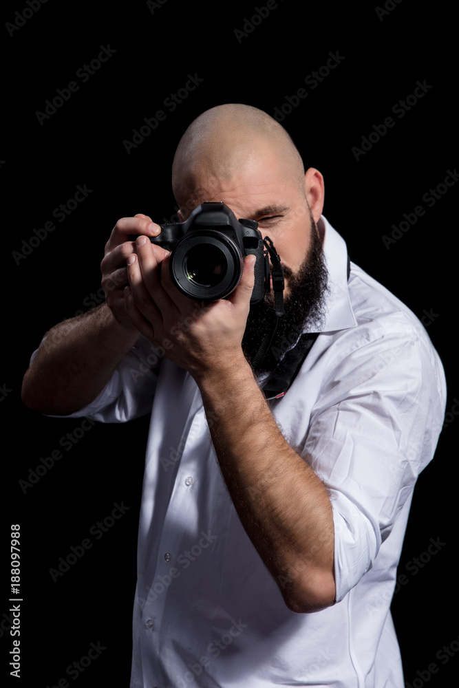 Photographer with camera. Male photographer with beard in a white shirt taking photon over black background Photographer with camera. Male photographer with beard in a white shirt taking photon over black background
