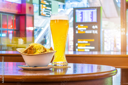 A glass of beer and a plate of breadcrumbs and cheese. In the background, online board displays flights to the airport. Concept expecting a voyage trip in a cafe, bar, retsorane drinking drinks.
