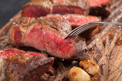 Closeup ready to eat steak new York beef breeds of black Angus with herbs, garlic and butter on a wooden Board. The finished dish for dinner. The finished piece of steak skewered on a fork photo