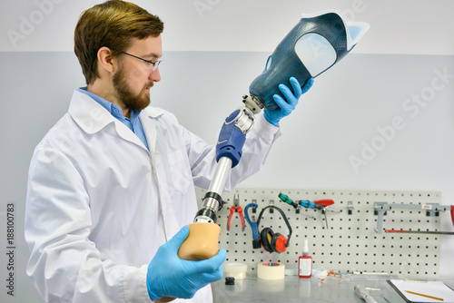 Portrait of young  prosthetics technician holding prosthetic leg  checking it for quality and making adjustments while working in modern laboratory, copy space photo