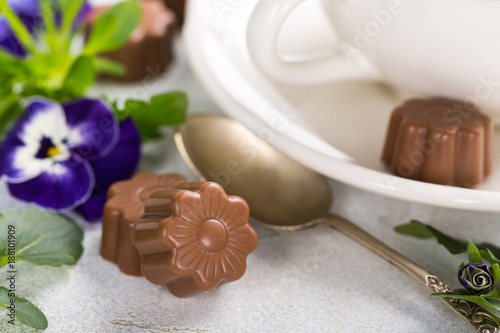 Chocolate candies in flower shape with violets and cup of coffee. Holiday food concept.