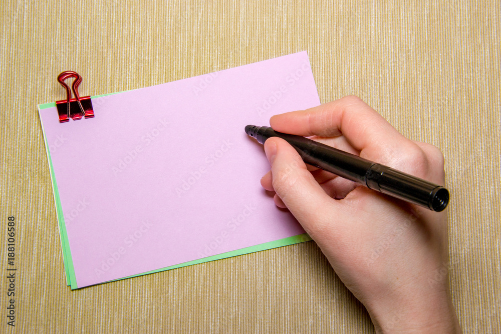 pink paper with paperclip and woman hand holding a pen about to write. Objects isolated on yellow pink paper with paperclip and woman hand holding a pen about to write. Objects isolated on yellow