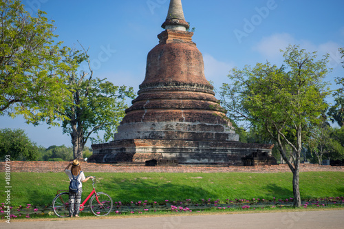 Young woman traveler travelling by bicycle into Wat Mahathat temple in the Sukhothai Historical Park contains the ruins of old Sukhothai, Thailand, UNESCO world Heritage Site.