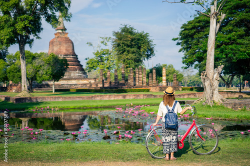 Canvas Print Young woman traveler travelling by bicycle into Wat Mahathat temple in the Sukhothai Historical Park contains the ruins of old Sukhothai, Thailand, UNESCO world Heritage Site