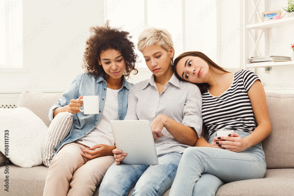 Three happy female friends using tablet and drinking coffee