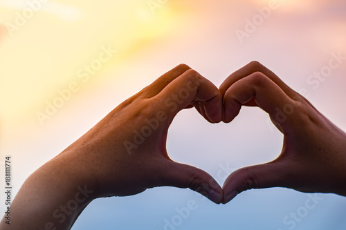 Woman Fingers in heart shape against colourful sunset sky. Valentine concept
