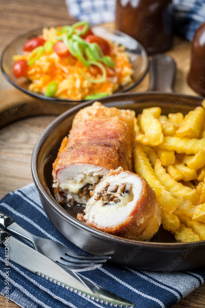Fried chicken breast stuffed with mushrooms and cheese wrapped in ham served with fries and salad. Fried chicken breast stuffed with mushrooms and cheese wrapped in ham served with fries and salad.