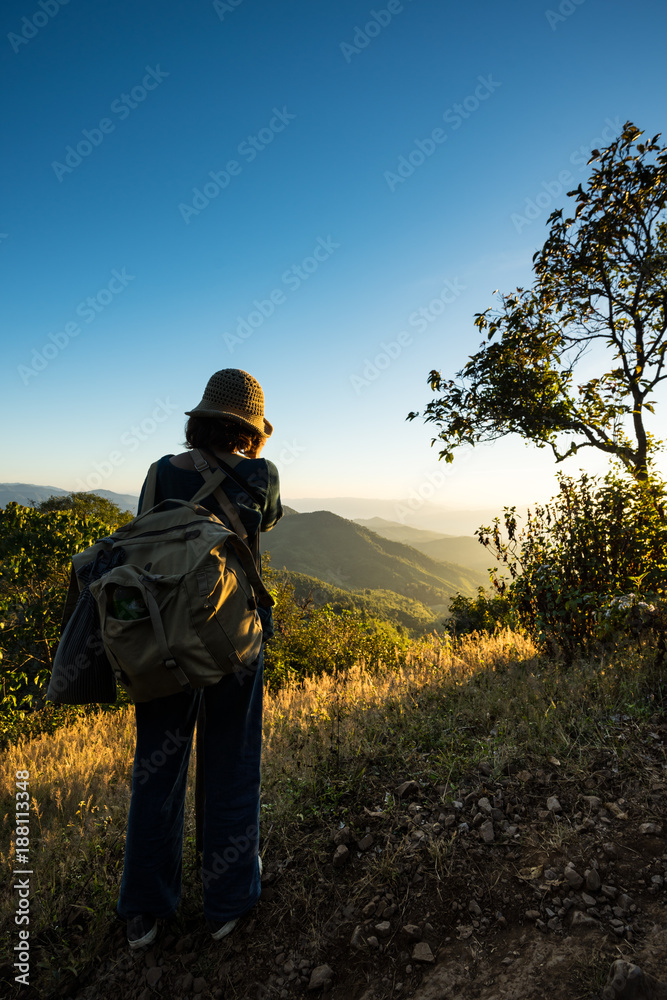Young woman backpacker watching sunset and beautiful view of Doi Pui Co, Mae Hong Son, Thailand. Sunset and blue sky over the mountains range. Camping and Adventure concept.