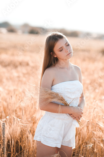Smiling teen girl 14-16 year old holding wheat posing in meadow. Posing outdoors. Summer season. 20s.