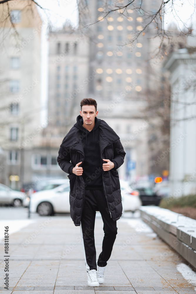 Stylish man wolk on the street. Winter cold outfit. Big jacket with white sneakers. Blured background street. Profecional model photo. Stylish man wolk on the street. Winter cold outfit. Big jacket with white sneakers. Blured background street. Profecional model photo.