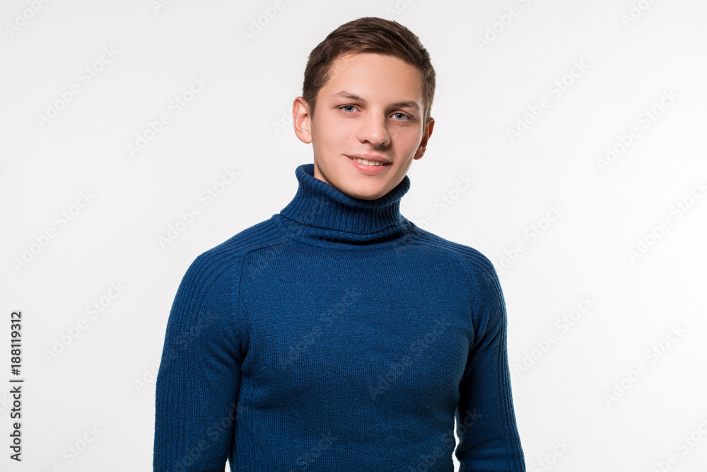 Studio shot of young man wearing blue turtleneck sweater against Studio shot of young man wearing blue turtleneck sweater against