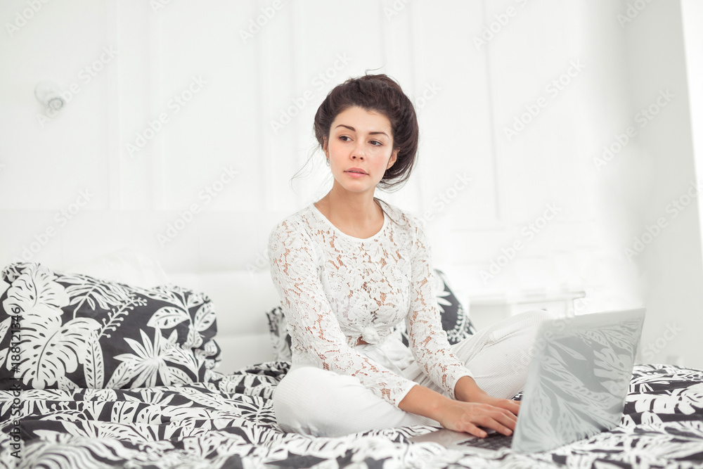 Young woman working with laptop at home, online business. Smiling woman sitting on bed, relaxing, browsing internet or online shopping, free time at home.