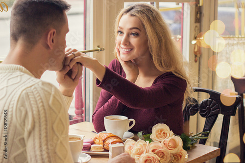 Back view man kissing his beloved woman hand while having romantic dinner in cozy french cafe. Happy young couple celebrating in vintage restaurant. Valentines day, love and togetherness concepts