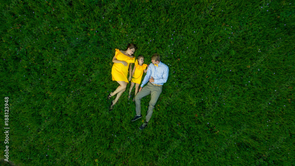 top view Happy family with one child concept - father, mother and child daughter . lying on the grass. yellow clothes. summer sunny day. in green nature together. Drone view.