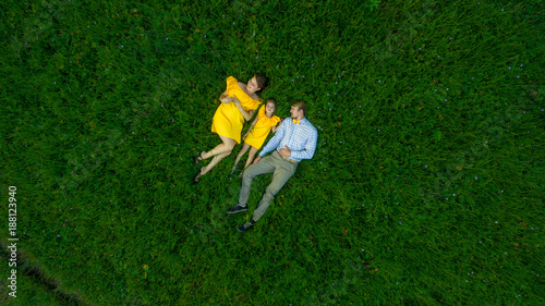 family lying on the grass. concept - father, mother and child daughter top view.. yellow clothes. summer sunny day. in green nature together. Drone view.