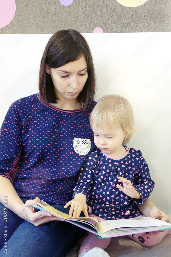 Fototapeta premium A young mother reads a children's book for a child.