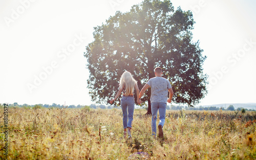 Loving couple running along the yellow grass against the background of a large tree © endrews21