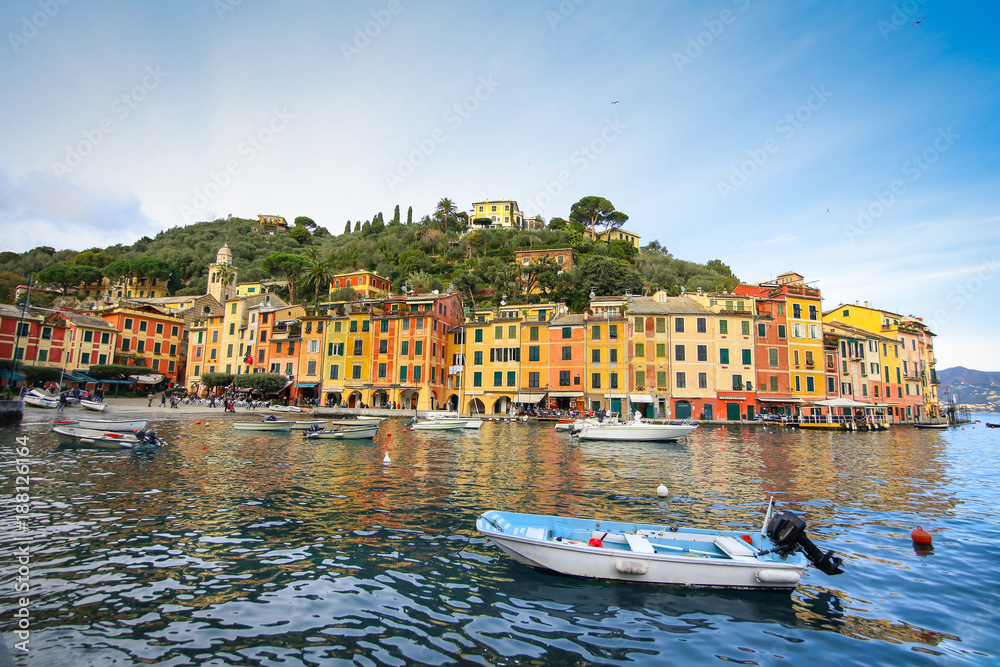 Colorful buildings on the promenade of Portofino with boats floating in the marina and blue sky background