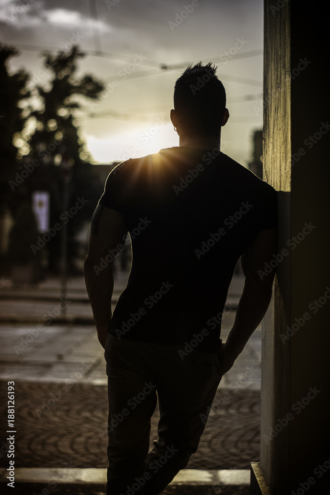 Backlit portrait of back of muscular man posing in European city center, Turin, Italy
