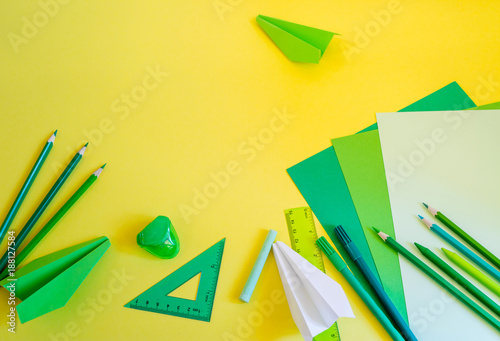 Creative, fashionable, minimalistic, school or office workspace with green supplies on yellow background. Flat lay.