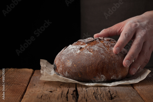 Closeup of male hands put fresh bread on an old rustic table on black background with copy space for your text