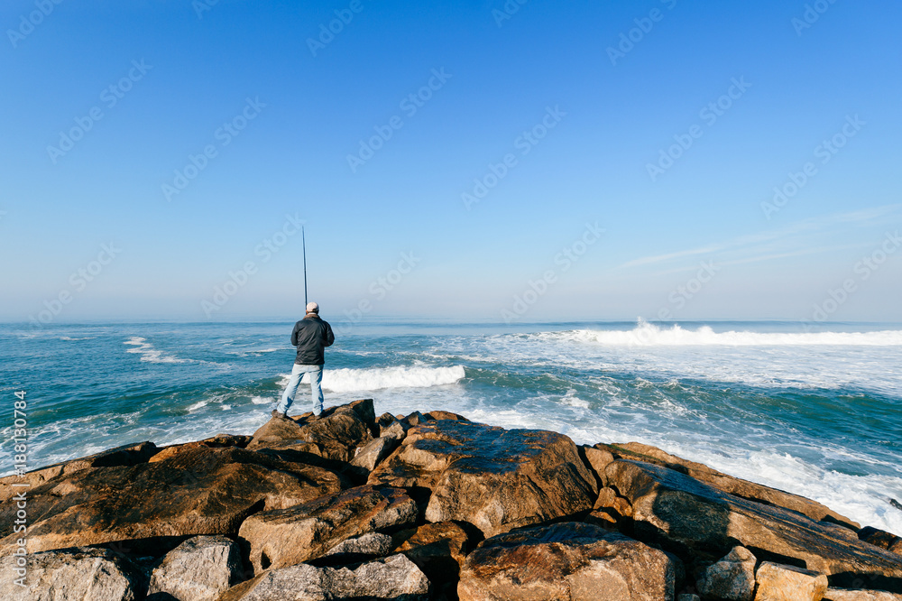 Lonely fisherman looking farmale and fishing with spinning at atlantic ocean cape in sunny windy morning outdoors. Beautiful seascape. Fishing rod and gear. Saulty aquatic breeze. Hobby and leisure.