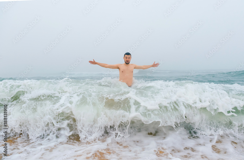 Odd bizarre crazy fearless awesome adult man enjoying in cold stormy sea. Guy jumping in waves in ocean with emotional funny face. Adult male fooling like child in water outdoors. Leisure activities Odd bizarre crazy fearless awesome adult man enjoying in cold stormy sea. Guy jumping in waves in ocean with emotional funny face. Adult male fooling like child in water outdoors. Leisure activities