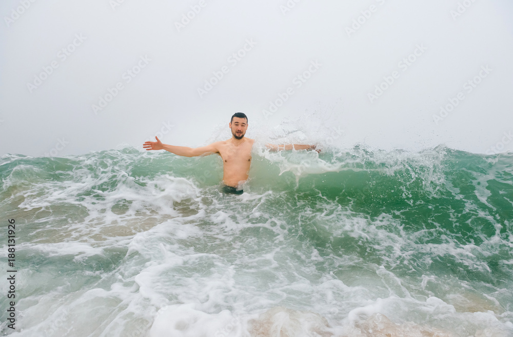 Odd bizarre crazy fearless awesome adult man enjoying in cold stormy sea. Guy jumping in waves in ocean with emotional funny face. Adult male fooling like child in water outdoors. Leisure activities