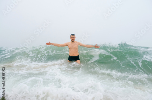 Odd bizarre crazy fearless awesome adult man enjoying in cold stormy sea. Guy jumping in waves in ocean with emotional funny face. Adult male fooling like child in water outdoors. Leisure activities