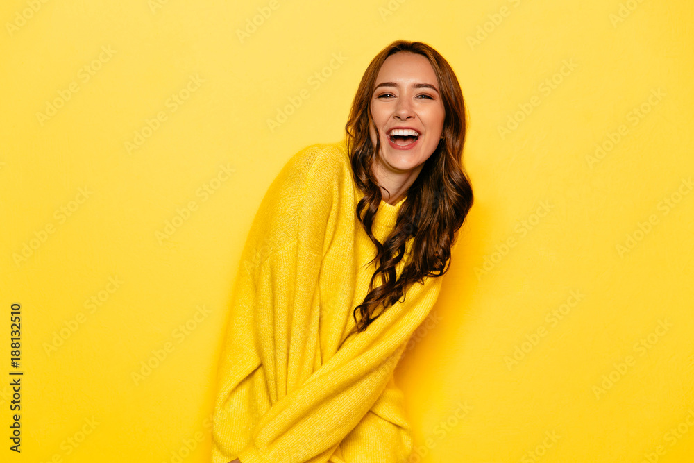 Excited young woman with curly hair in yellow sweater, widely smiling, looking at camera. Isolated on yellow background. Excited young woman with curly hair in yellow sweater, widely smiling, looking at camera. Isolated on yellow background.
