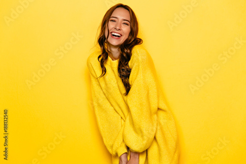 Funny young woman with curly hair in yellow sweater, widely smiling,. Isolated on yellow background.