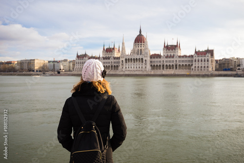 Young woman is standing on the riverbank of the Danube river and looking at Hungarian Parliament Building in BudaPest, Hungary © blazekg