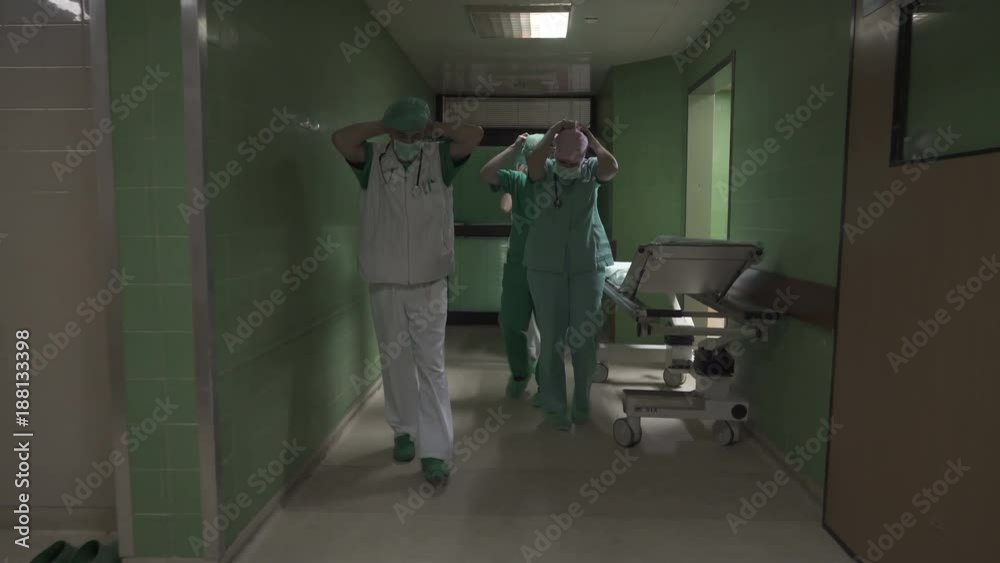 Male and female doctors specialist with medical technicians putting protective masks and walking through the hallway of hospital operation ward to examining patients before surgery,tracking,steady cam Male and female doctors specialist with medical technicians putting protective masks and walking through the hallway of hospital operation ward to examining patients before surgery,tracking,steady cam