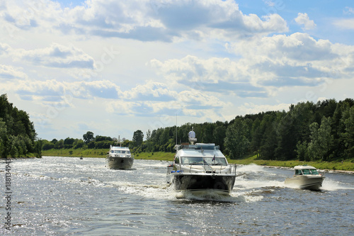 A few luxurious pleasure boats slowly cruising the river against the blue sky. Sunny day