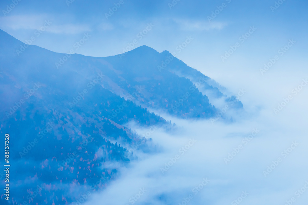 mountain landscape with fog below the peaks and clouds above them in blue tones