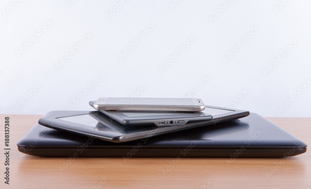 Stack of electronic gadgets on a table - notebook, tablet, ebook reader and a smatphone on the top Stack of electronic gadgets on a table - notebook, tablet, ebook reader and a smatphone on the top