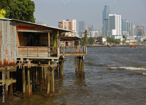 Bangkok, Thailand - 04 11 2017: Ancient wooden Construction on Poles at the Chao Praya River, modern High Rises in Background