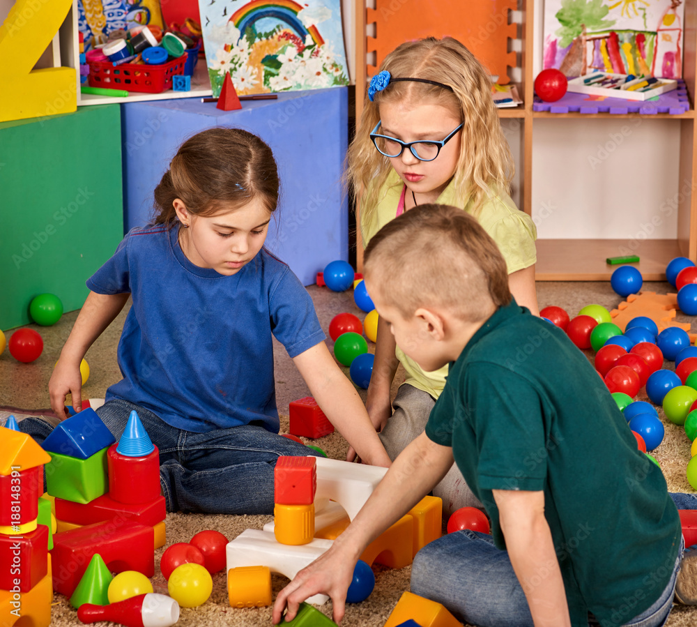 Children building blocks in kindergarten. Group kids playing toy on floor.  Interior preschool. Kid is keen on playing dice. Game of block replaces  games on smartphone. фотография Stock | Adobe Stock