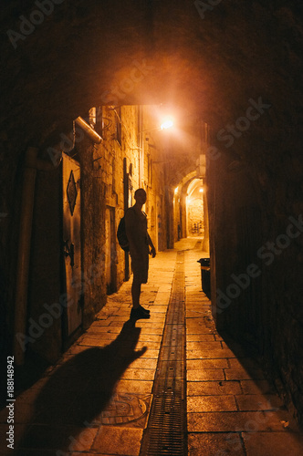 Illuminated cobbled street with light reflections on cobblestones in old historical city by night. Dark blurred silhouette of person goes in search of adventure in Old Jaffa in Tel-Aviv, Israel