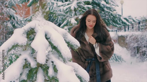 Close-up of Brunette fashionable sexy pretty rich woman in brown fur coat brushes woman walking in winter time slow motion. Happy girl having fun in snow. Snow covered Christmas trees in the winter