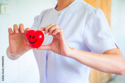 A nurse holding red heart toy. She is Left / right hand holding it.The photo shows the principle of caring and good health.