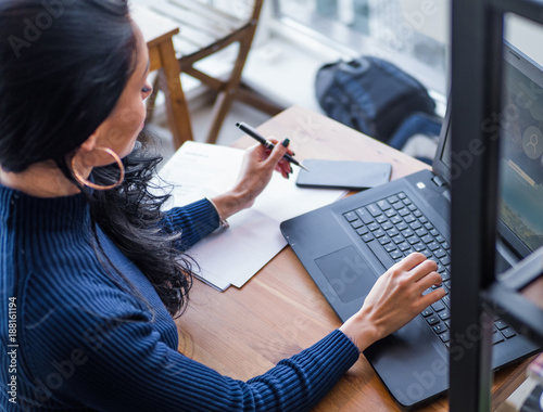 Young female student studying in the coffee shop with laptop, asian female student doing report or thesis in the cafe, front view of female studying at coffee shop sitting at wooden table. photo