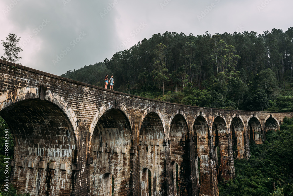 Loving couple on the edge of the bridge. Guy and girl traveling around Asia. The couple travels to Sri Lanka. Man and woman in an unusual place. Nine-arch bridge. Travellers in Asia. Hold hands