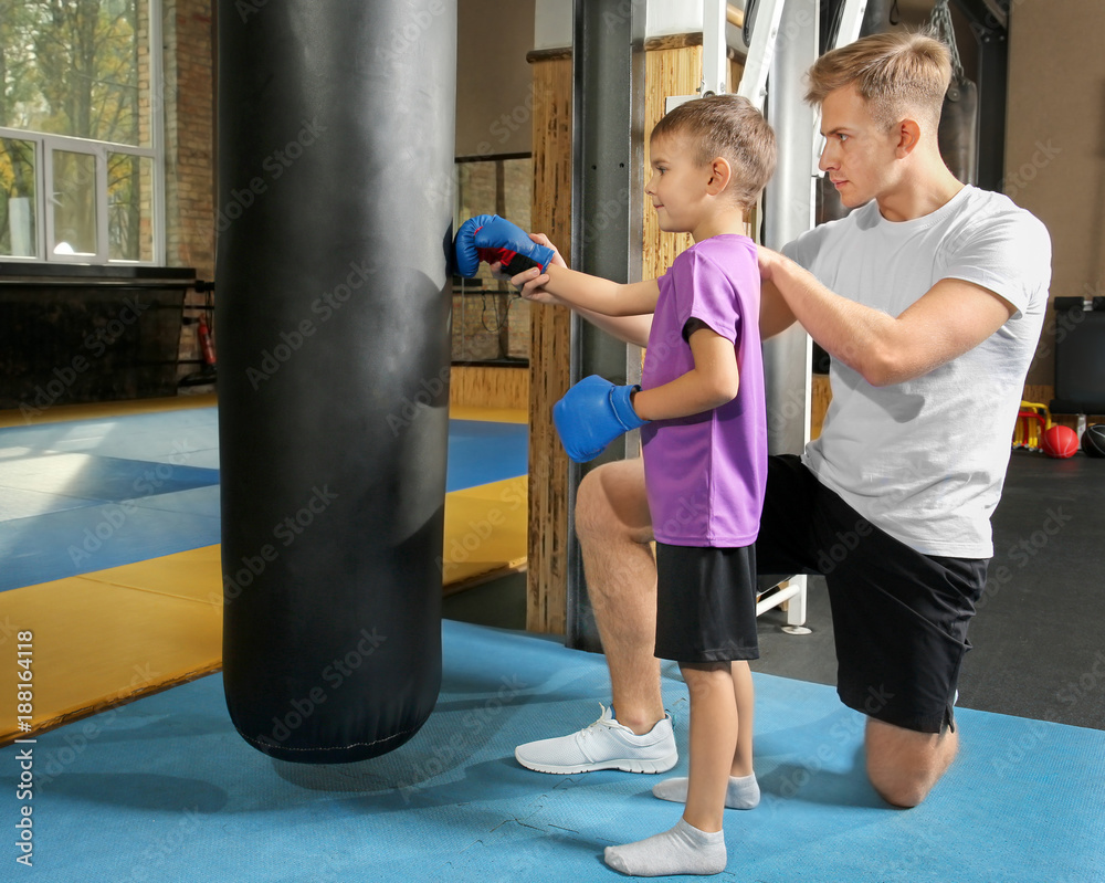 Little boy with trainer near punchbag in gym