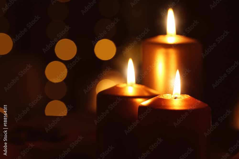 Beautiful burning candles in darkness against defocused lights
