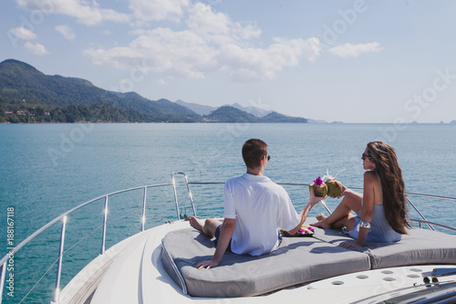 couple enjoying honeymoon onboard of luxury boat, luxurious yacht in tropical sea, man and woman drinking coconuts and relax