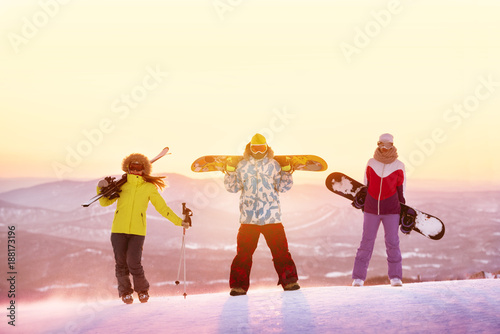 Ski or snowboard concept with three friends against sunset