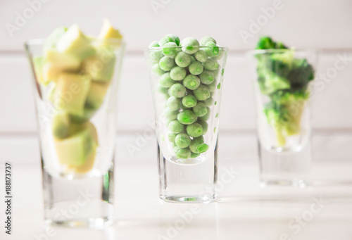 Assortment of green cut vegetables in shot glass on white background.